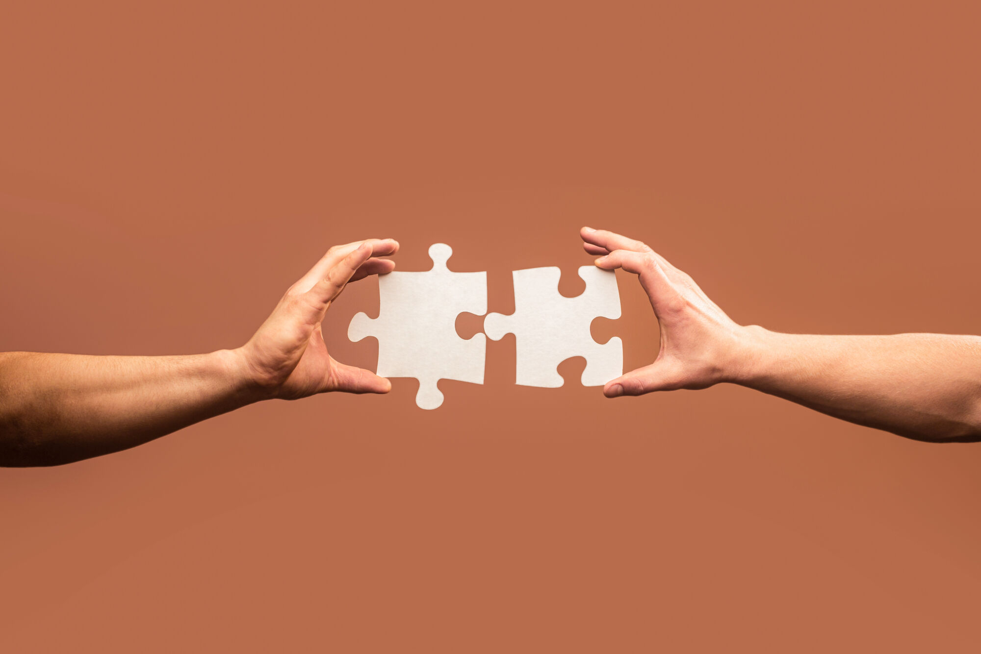 business solutions, success and strategy concept. Two hands trying to connect couple puzzle piece on gray background. Teamwork concept. Closeup hand of connecting jigsaw puzzle